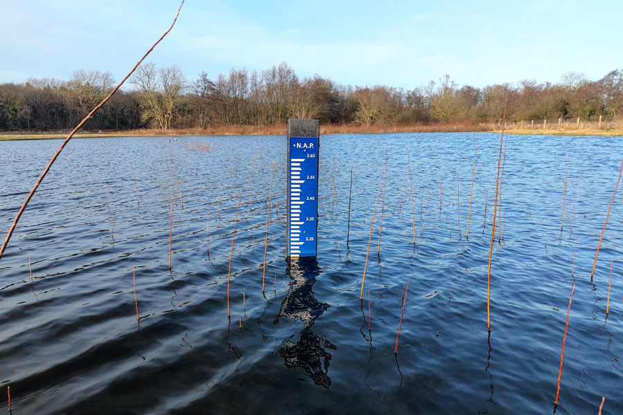 Afbeelding van hoog water in een meer met een bordje dat het waterpeil aangeeft tov nap